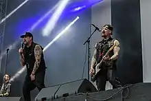 Joel Madden in the center signing into a microphone, and Benji Madden on the right playing guitar