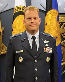 Air Force Brigadier General Jeffrey Cashman in uniform, standing before flags at his promotion ceremony, 2015