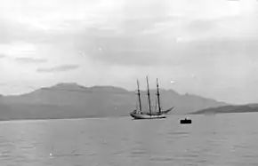 A black and white photograph of a sailing ship in a bay