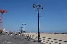 Original street lights, similar to those installed on Fifth Avenue in Manhattan. They consist of stylized black poles with two lamps at the top. The boardwalk is on the left and the beach is on the right.