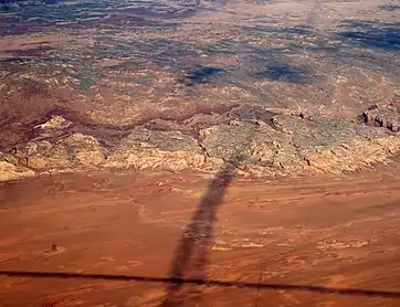 Shadows of contrails over San Rafael Reef —San Rafael Swell, Reef (perimeter), and San Rafael Desert at south & southeast. The Reef is most of the southeast, and east perimeter of the 45-mile-wide (72 km) (west-to-east) San Rafael Swell, which trends southwest-by-northeast.