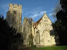 To the left is a battlemented tower, in the middle a ruined wall, and to the right the end of a stone chapel with a red tiled roof