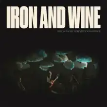 A band on a dark stage with a projection of clouds behind them, with the words "Iron and Wine" and album title superimposed