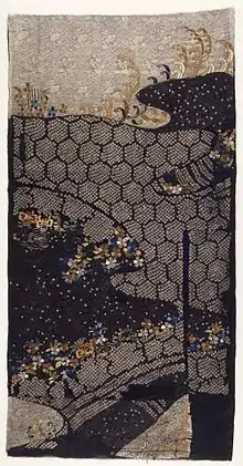 A rectangular length of cream fabric, appearing to be relatively fragile in places, half of it dyed a dark navy-blue. In places, the fabric has torn with age, and there are some sections of the fabric entirely missing.