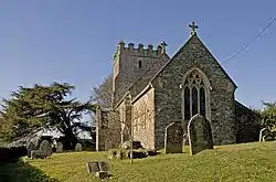 Stone building with square tower. In the foreground are gravestones.
