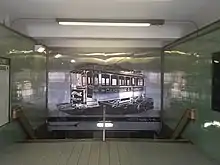 Interior of a subway entrance, with a mural of a streetcar on a reflective panel