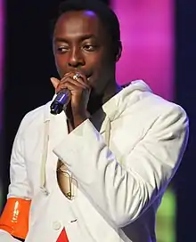 An African-American man wearing a white jacket sings into a microphone.