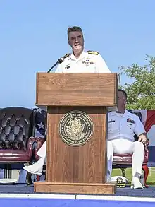 Colour photo of a man wearing a white uniform standing behind a lectern